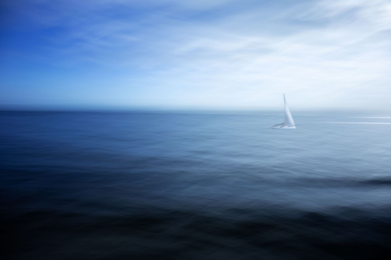 Minimalist seascape with a single white sailboat on a serene blue ocean horizon.