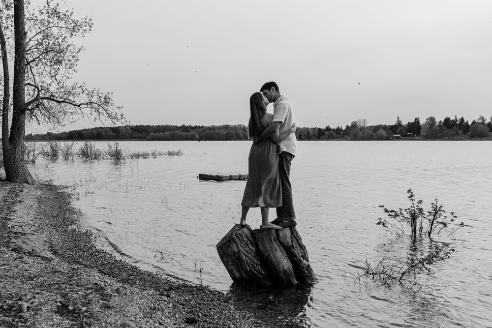 A couple shares romantic moments along a tranquil lakeshore.