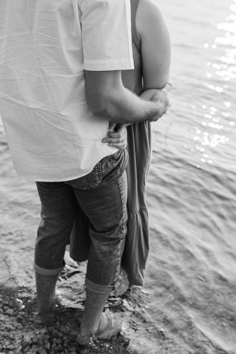 Black and white photo showing legs of a couple standing in shallow water.