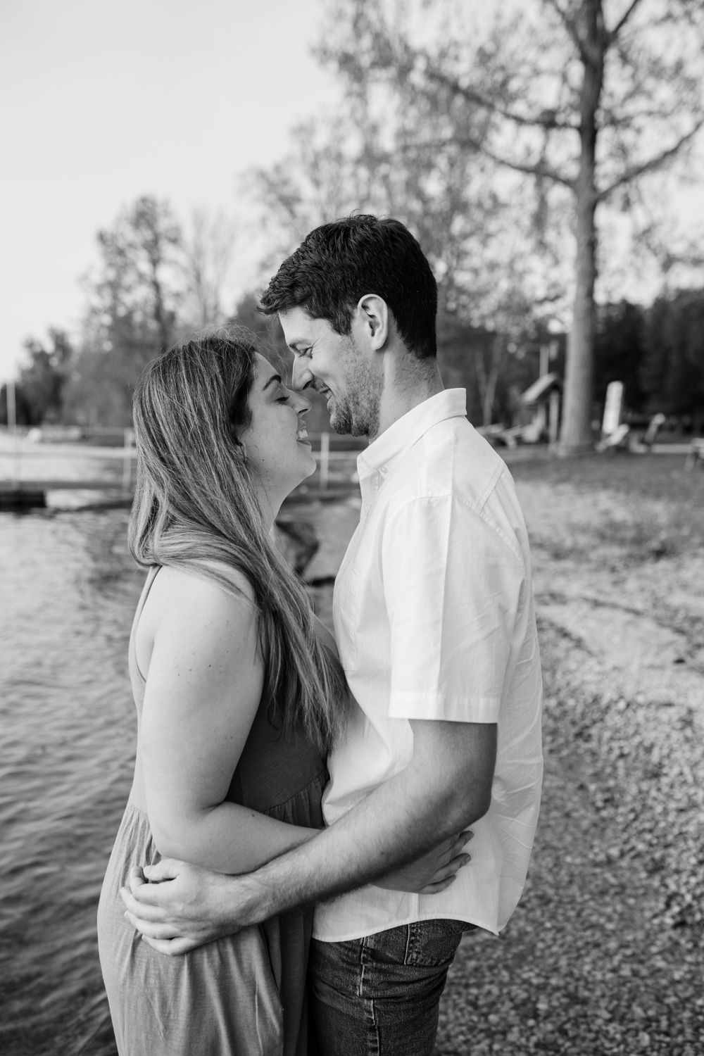 A romantic black and white photoshoot by the water shows an intimate couple embracing on a rocky shoreline.
