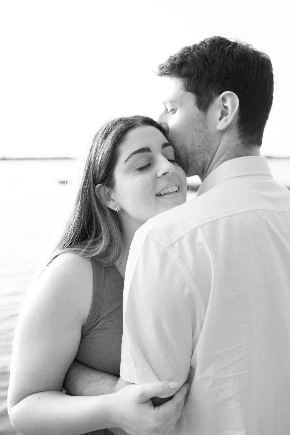 Intimate black and white portraits show a couple sharing close moments by the water.