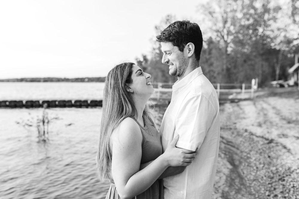 Black and white engagement photos capture tender moments between a couple near the water.