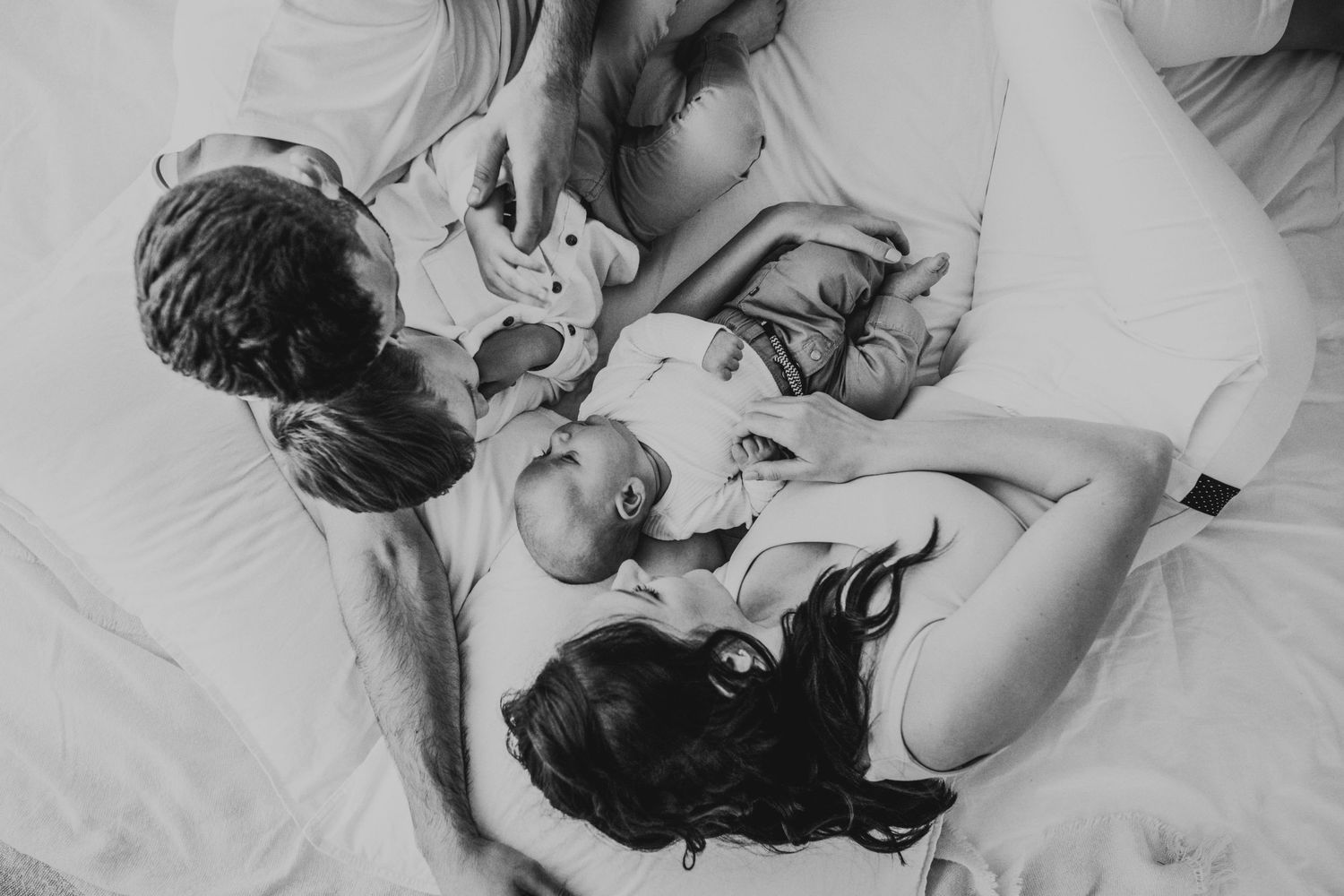 Black and white photo of a family sharing tender moment on white bedding.