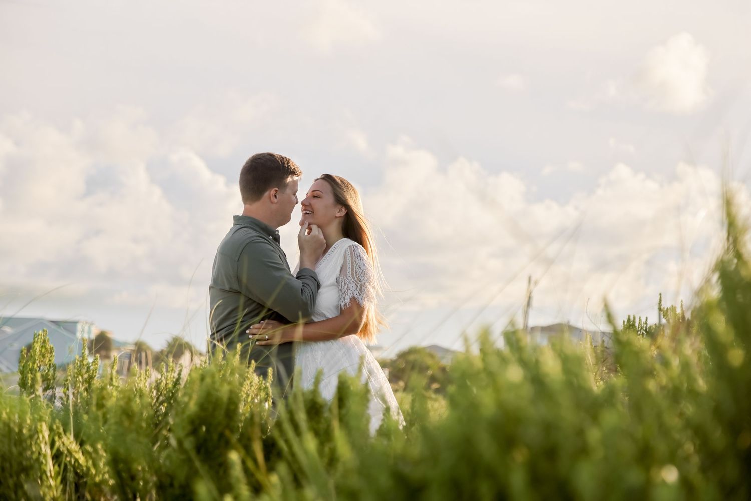 A tender embrace among tall grass and wildflowers during golden hour.