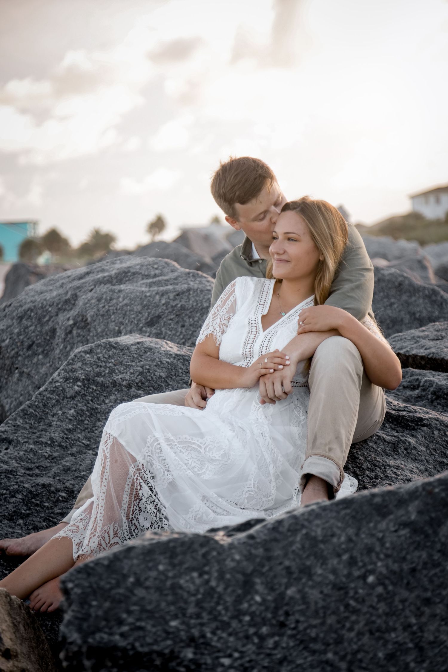An intimate moment shared on dark coastal rocks during sunset.