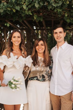 A group poses together outdoors wearing coordinated white and beige outfits in a garden setting.