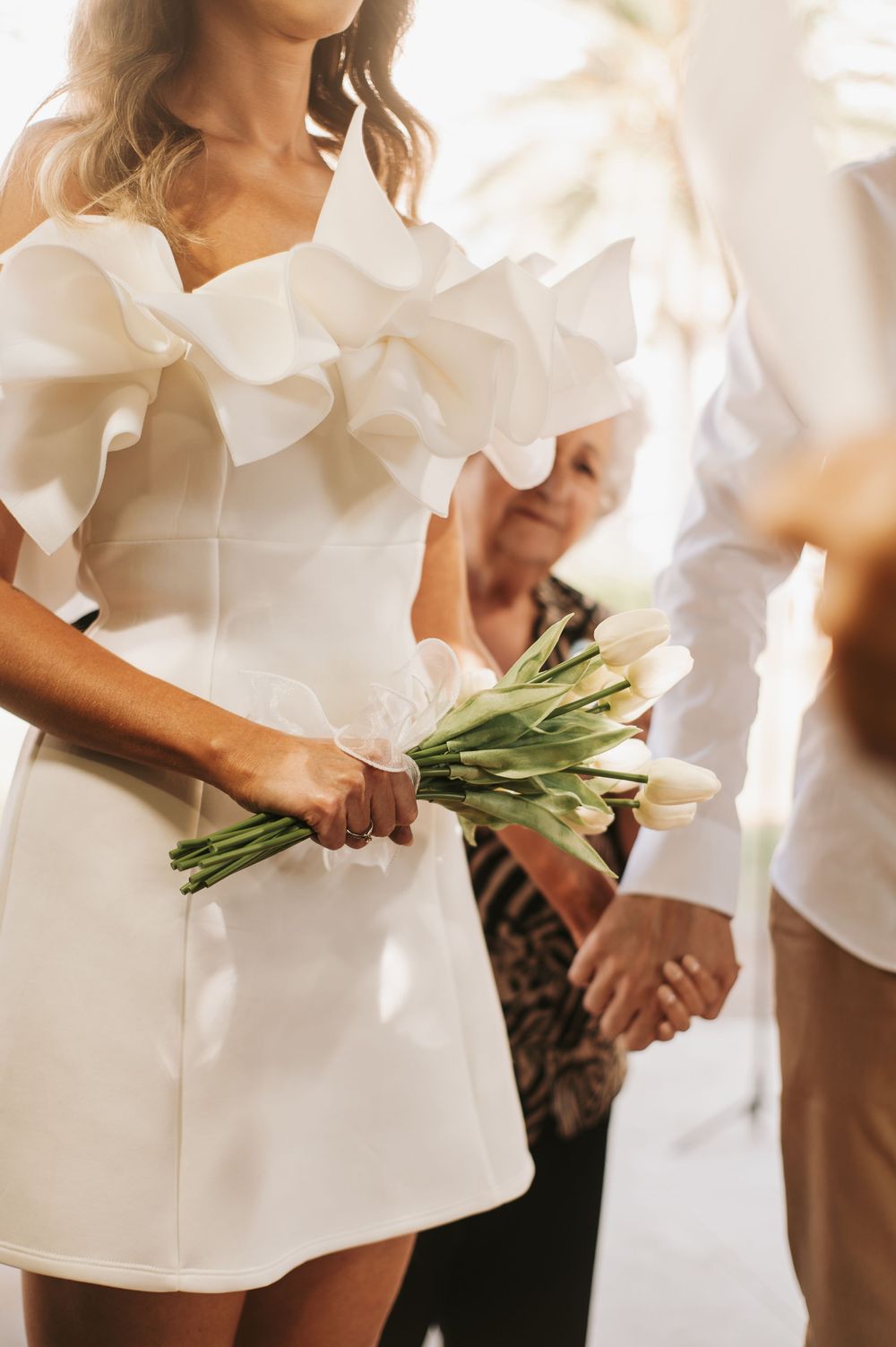 Person in white ruffled dress holding fresh greenery bouquet.