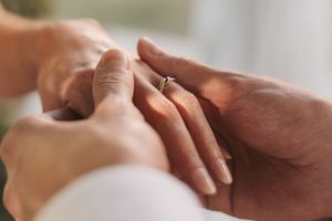 Close-up shot of hands placing engagement ring on finger.