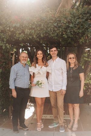 Wedding party poses under ivy-covered archway for formal group photo.