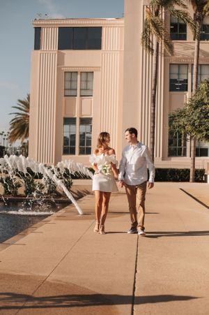 A couple walks hand in hand near a fountain outside an Art Deco style government building in San Diego.