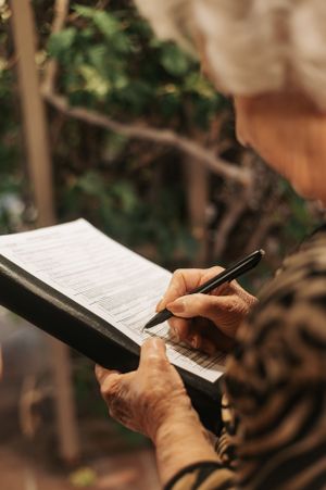 Person signing marriage certificate with pen during outdoor wedding ceremony.