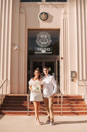 Couple poses outside the City of San Diego building entrance with classic architecture.