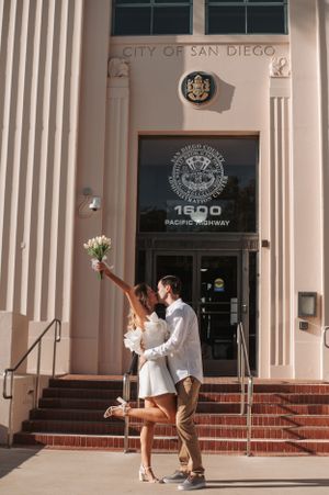 A couple celebrates at the City of San Diego building entrance with a celebratory bouquet toss on the steps.