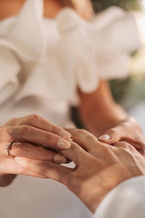 Close-up shot of hands exchanging wedding rings in natural sunlight.