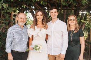 Small wedding group smiles for portrait under garden pergola with green foliage.