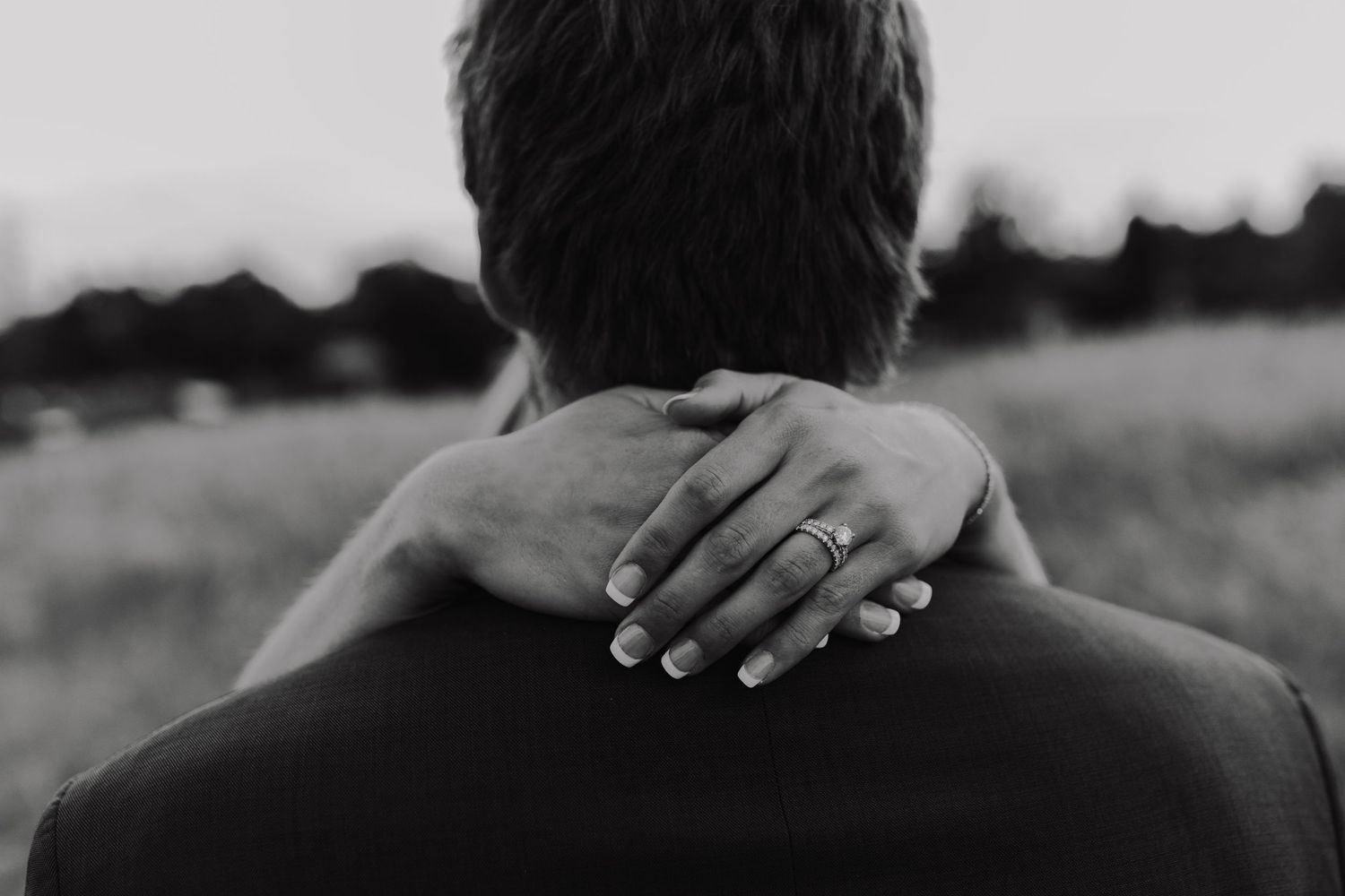 Close-up black and white photo of hands with wedding ring embracing from behind.