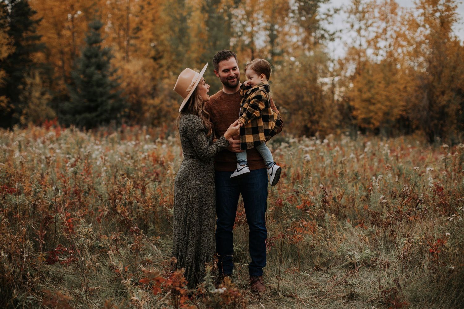 A family shares a tender autumn moment in a field with golden fall foliage.