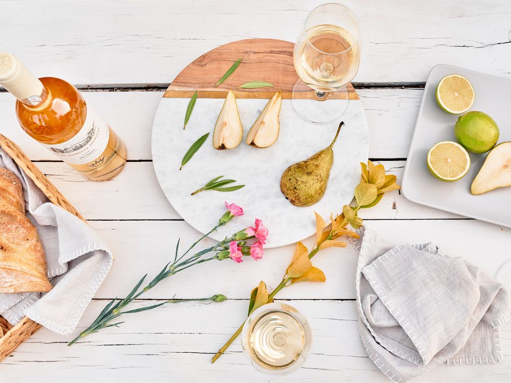 Elegant flatlay of white wine, pears, and flowers on rustic white wooden table.