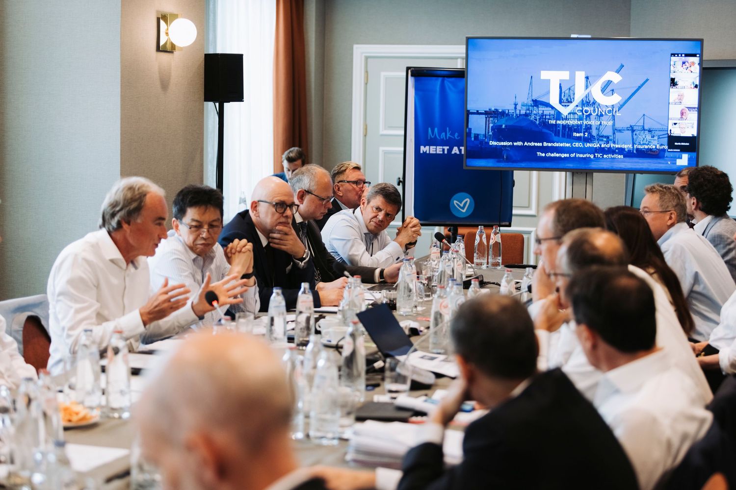 Business executives gathered around conference table watching presentation on TV screen.