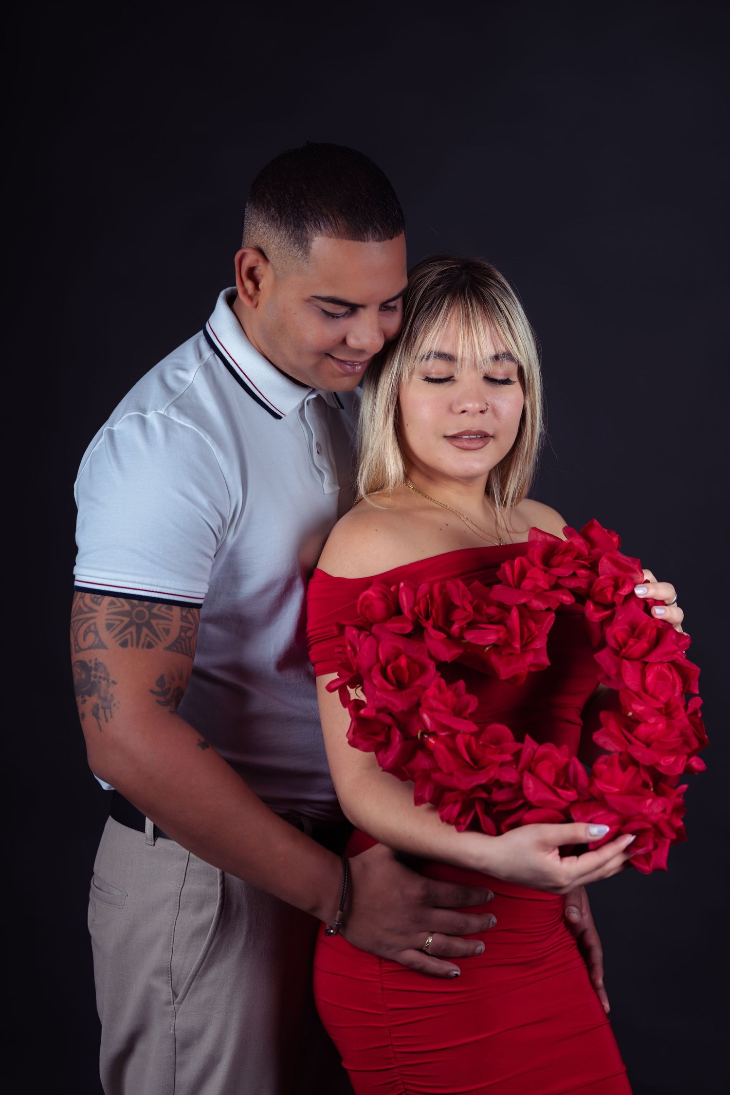 Romantic couple embracing with red roses against dark background.