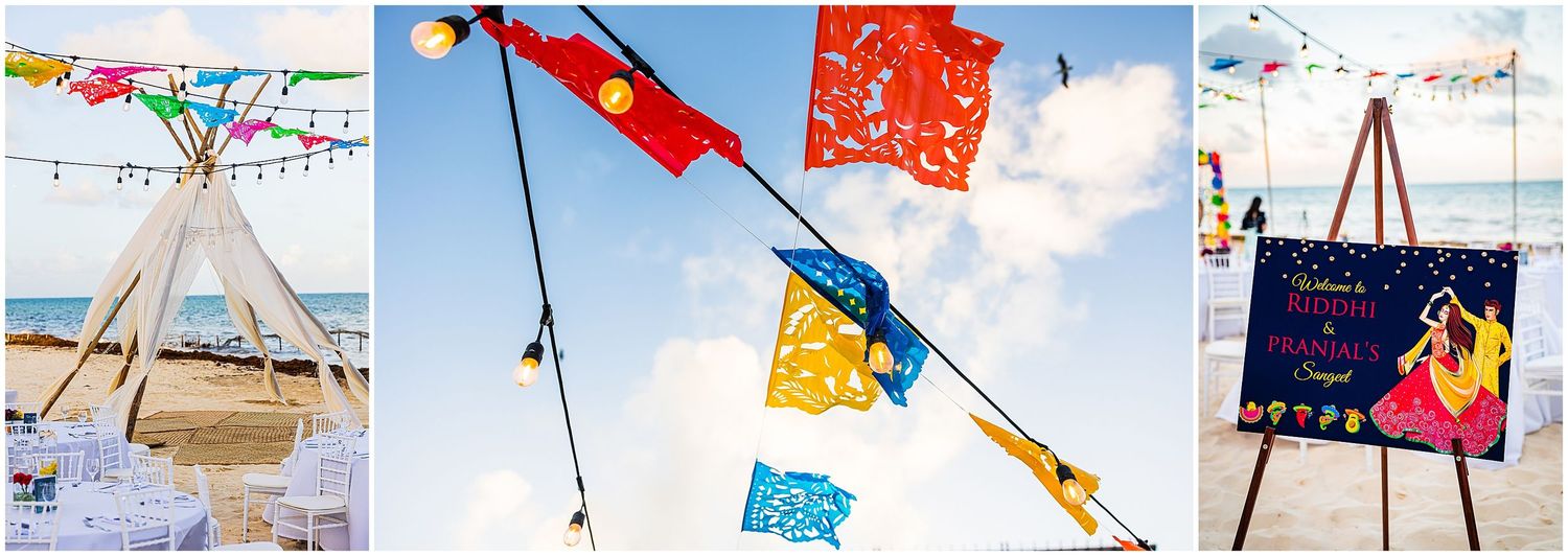 Beach wedding decor featuring colorful papel picado banners against blue sky.