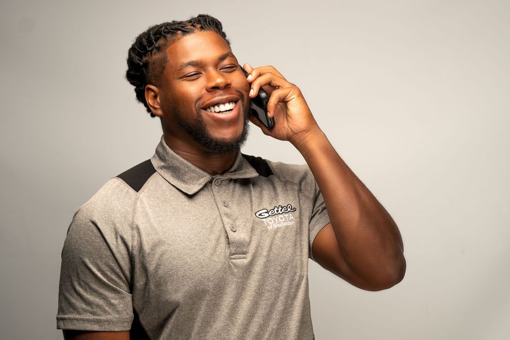 Smiling professional in grey polo shirt talking on mobile phone against neutral background.