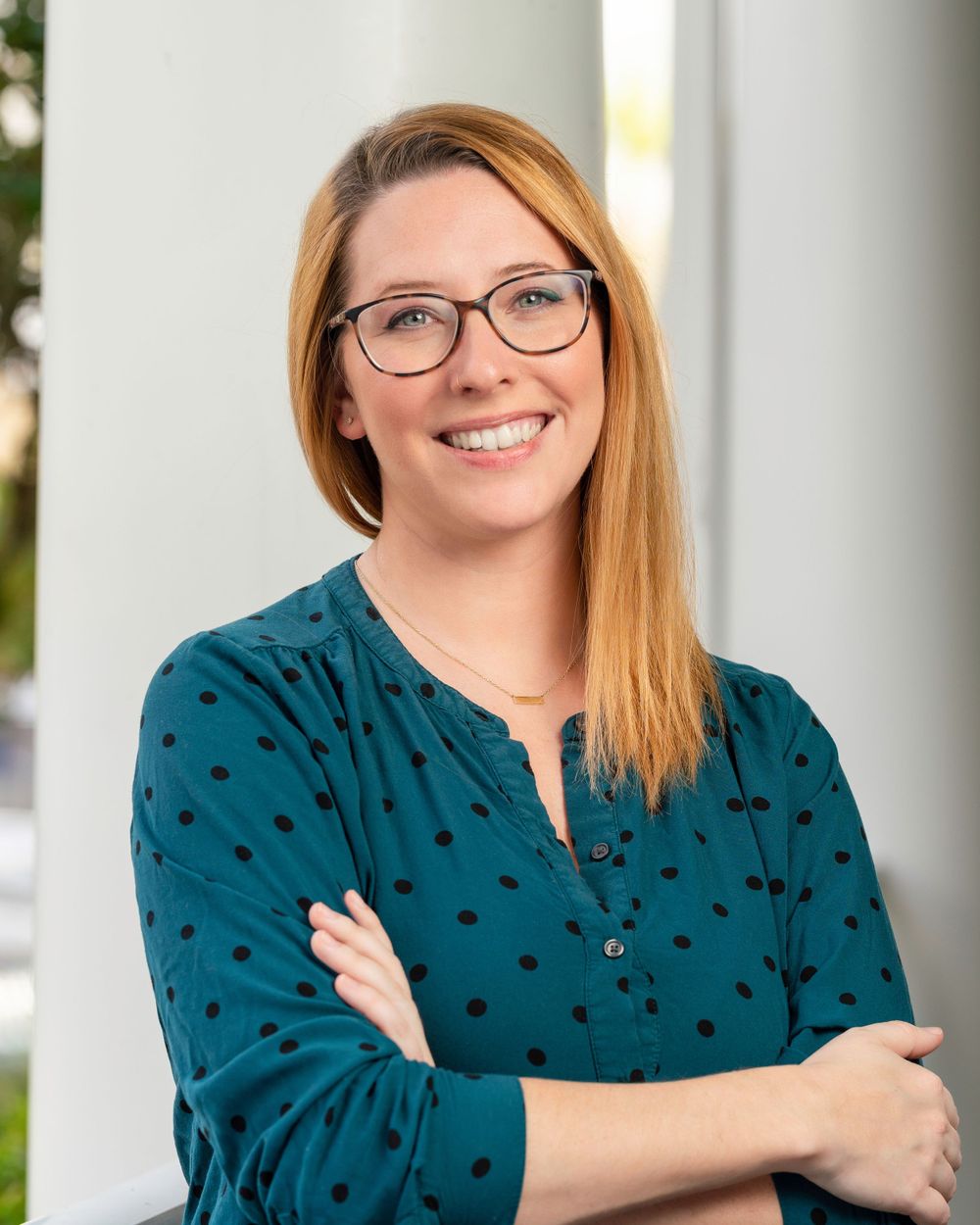 Professional headshot with glasses and polka dot blouse against white columns.