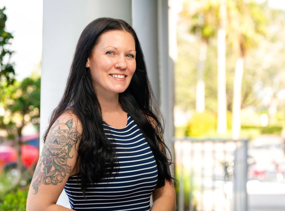 Casual outdoor portrait in striped top showing tattoo sleeve against white columns.