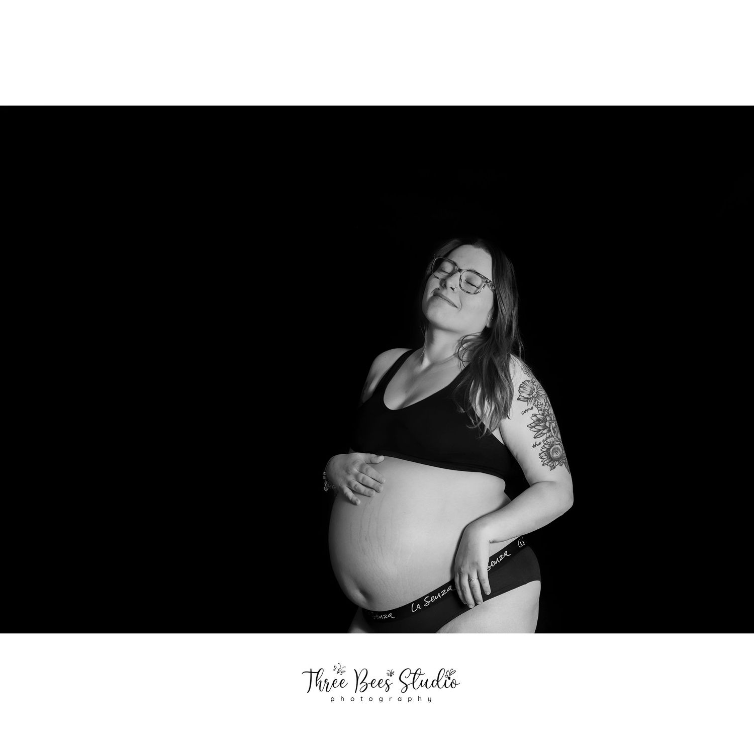 Black and white maternity portrait showcasing an expecting mother's belly against a dark background.