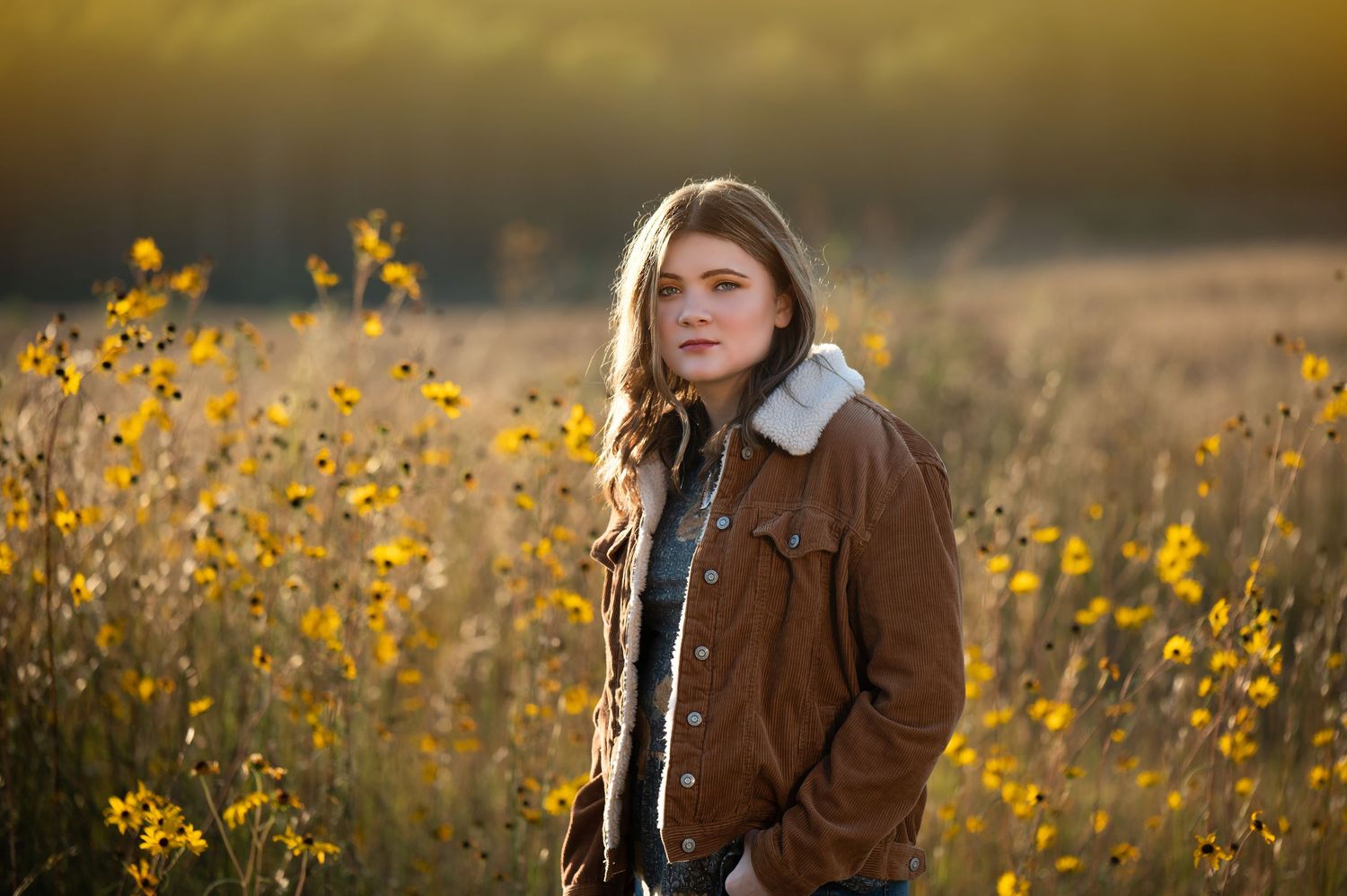 Person in brown jacket poses in field of yellow wildflowers during golden hour.