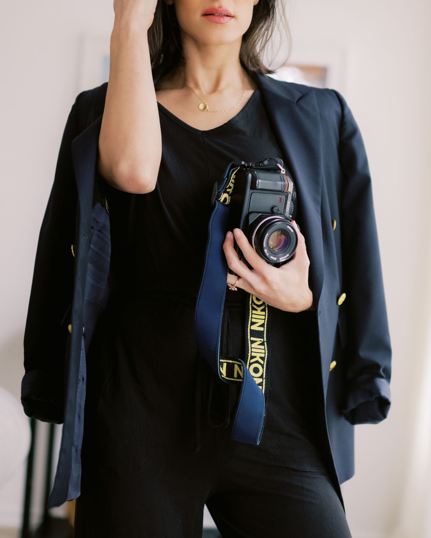 Photographer wearing black blazer and holding vintage camera with blue camera strap.