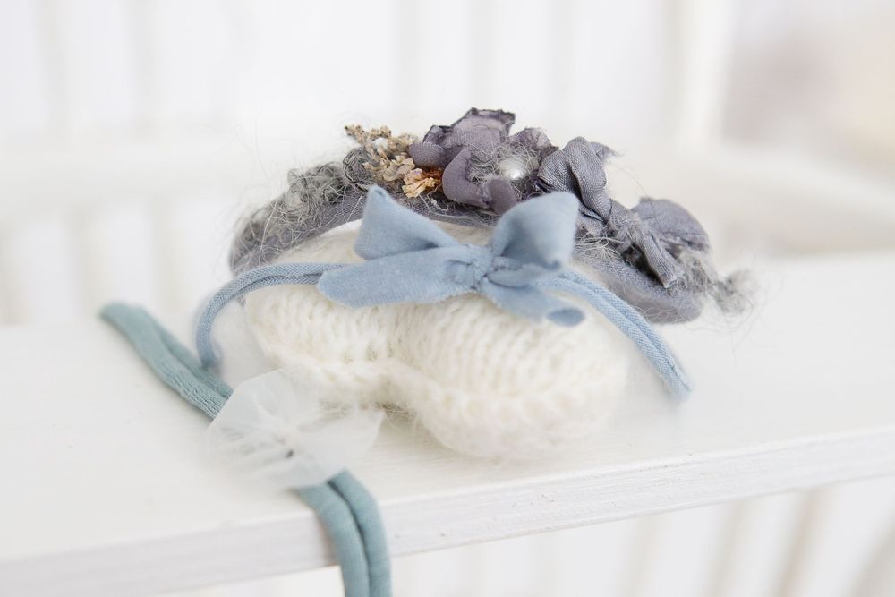Delicate blue and gray floral headpiece with ribbon details on white surface.