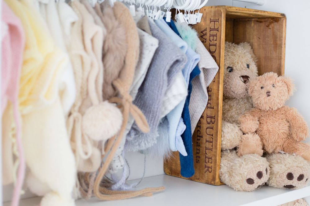 Baby clothes and plush teddy bears arranged neatly in a wooden display shelf.