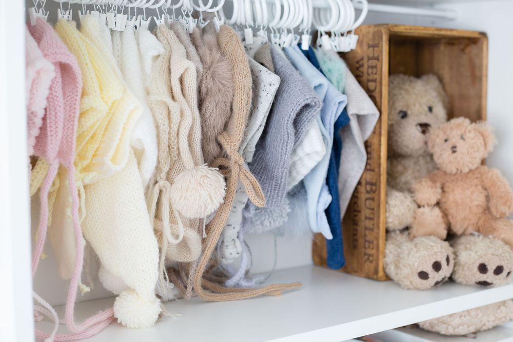 Organized closet with baby clothes in soft colors and plush teddy bears on display.