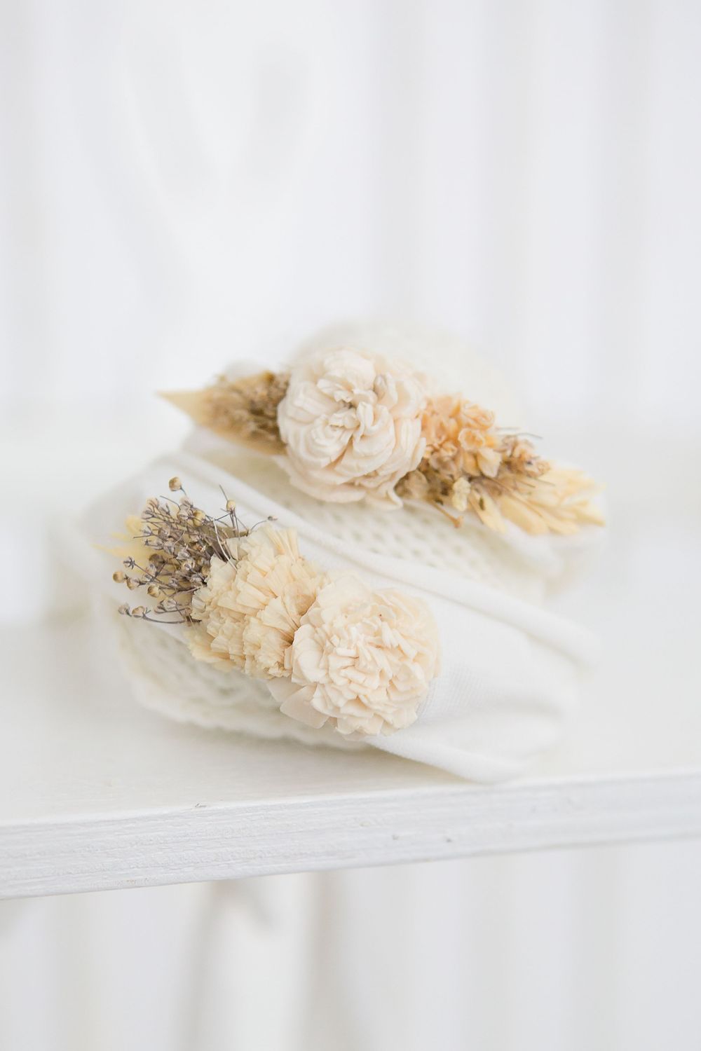 Dried floral hair accessories in cream and beige tones on white fabric.