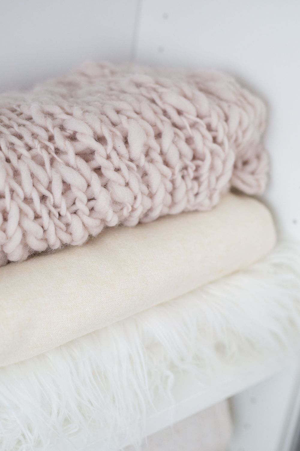 Stack of cozy textured blankets in soft pink and cream colors.