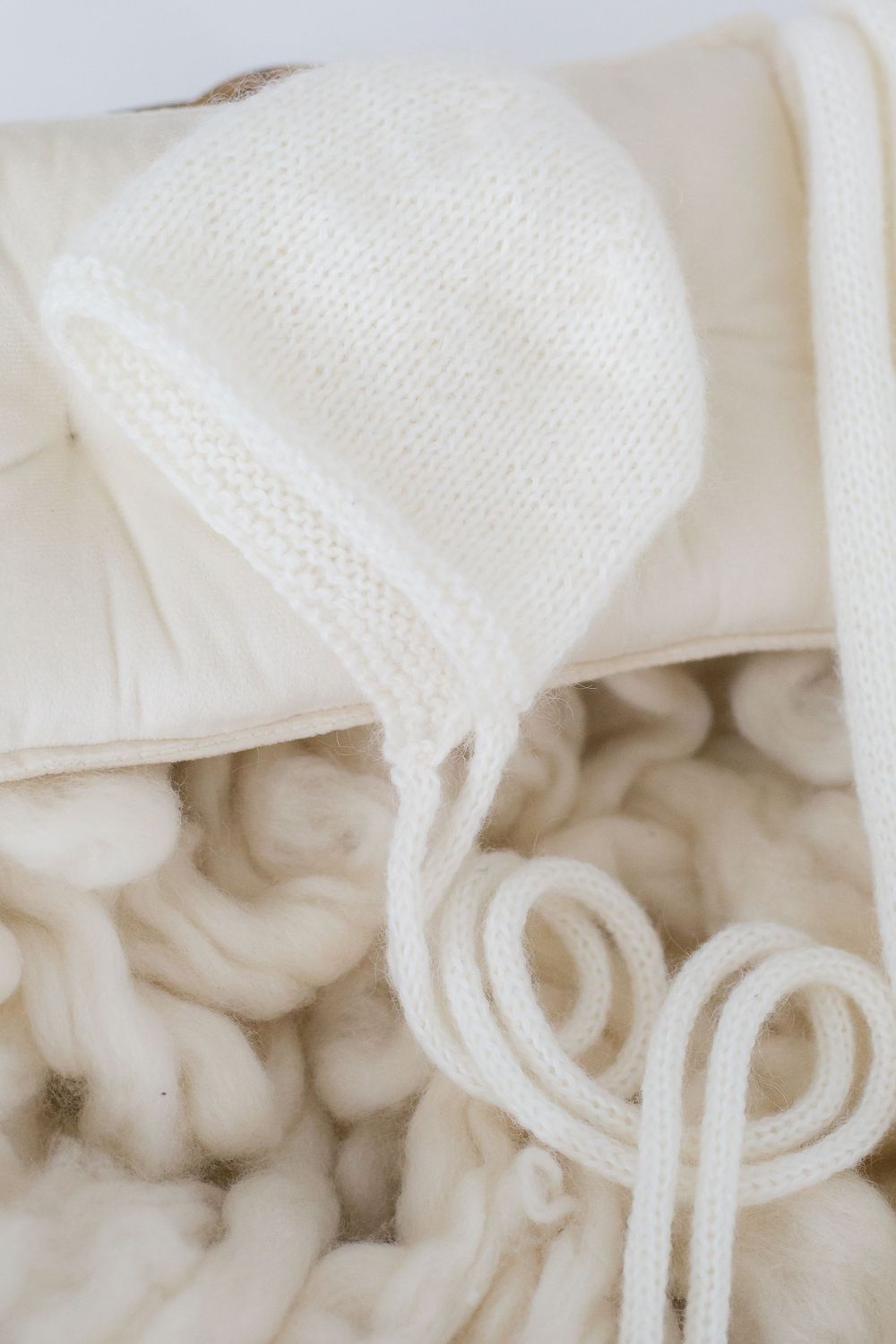 Close-up of white knitted baby bonnet with delicate details on soft fabric.