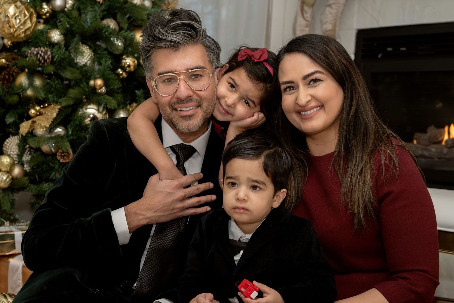 Family poses together near decorated Christmas tree during holiday photoshoot.