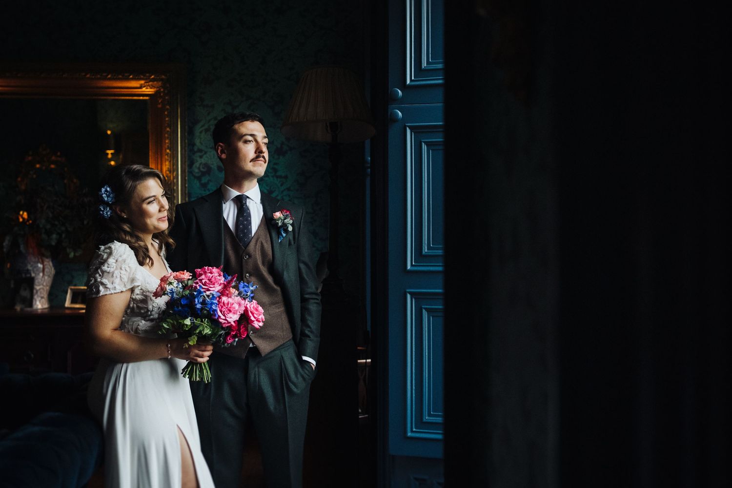 Dramatic lighting illuminates couple in formal attire against dark blue interior.