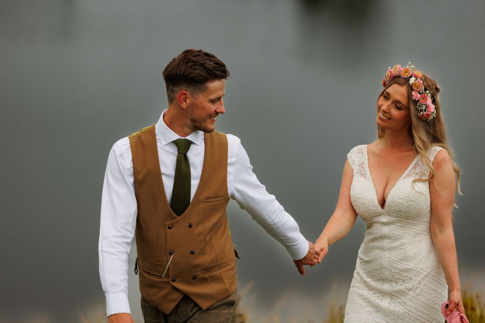 A couple in wedding attire walking hand in hand against a misty background.