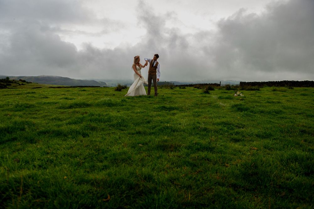 Romantic wedding portrait on green hillside with dramatic cloudy sky.