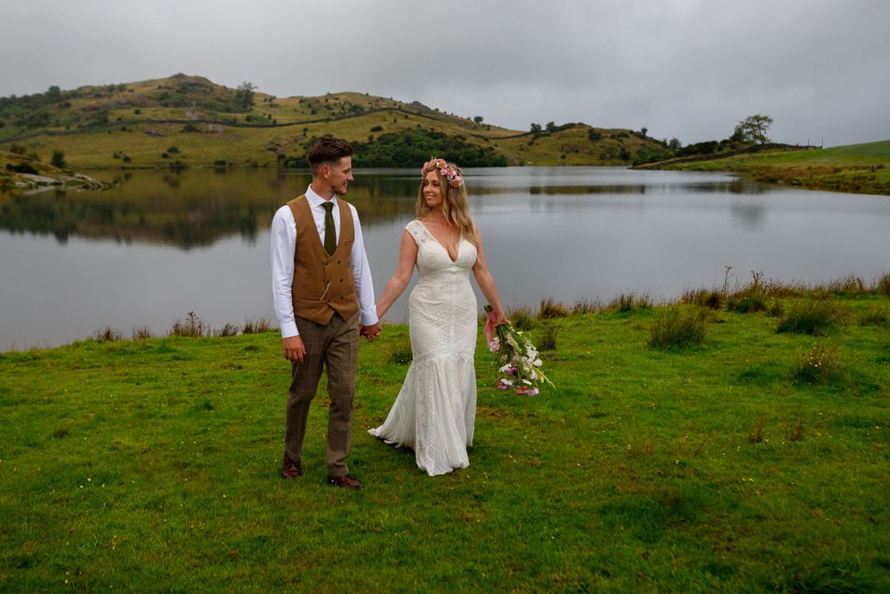 Bride and groom pose together near a peaceful lake with hills reflected in the calm water.