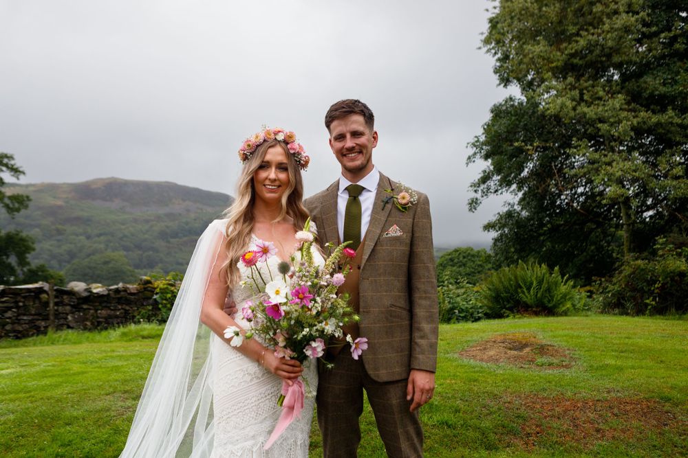 Wedding couple poses on grassy hillside with mountains visible in background.