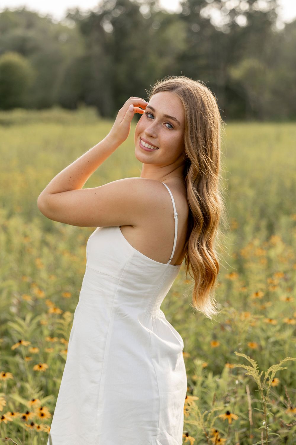girl standing in a field of wildflowers tucking her hair behind her ears