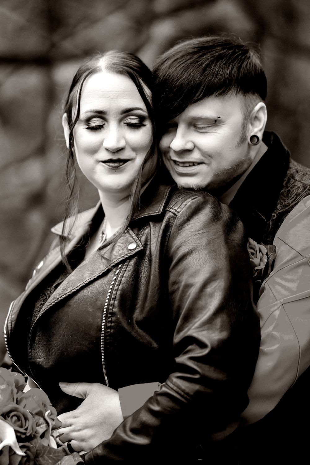 Bride in black dress and groom in black vest in A romantic black and white portrait of a couple in leather jackets.