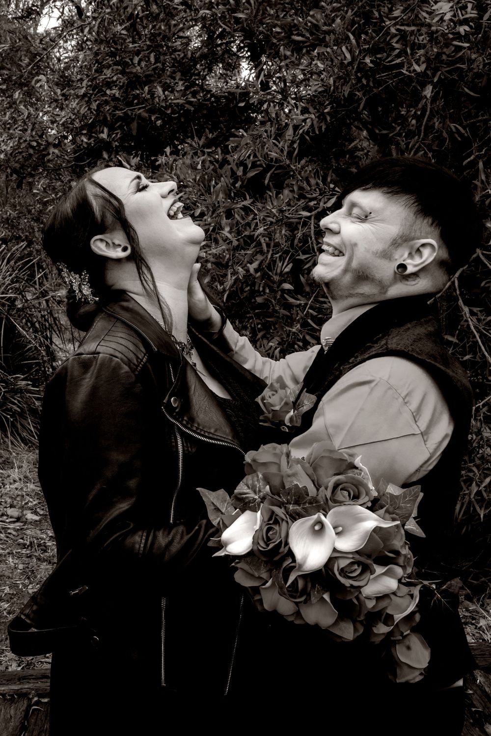 Bride in black dress and groom in black vest in Romantic portrait series in black and white with dramatic lighting and floral elements.