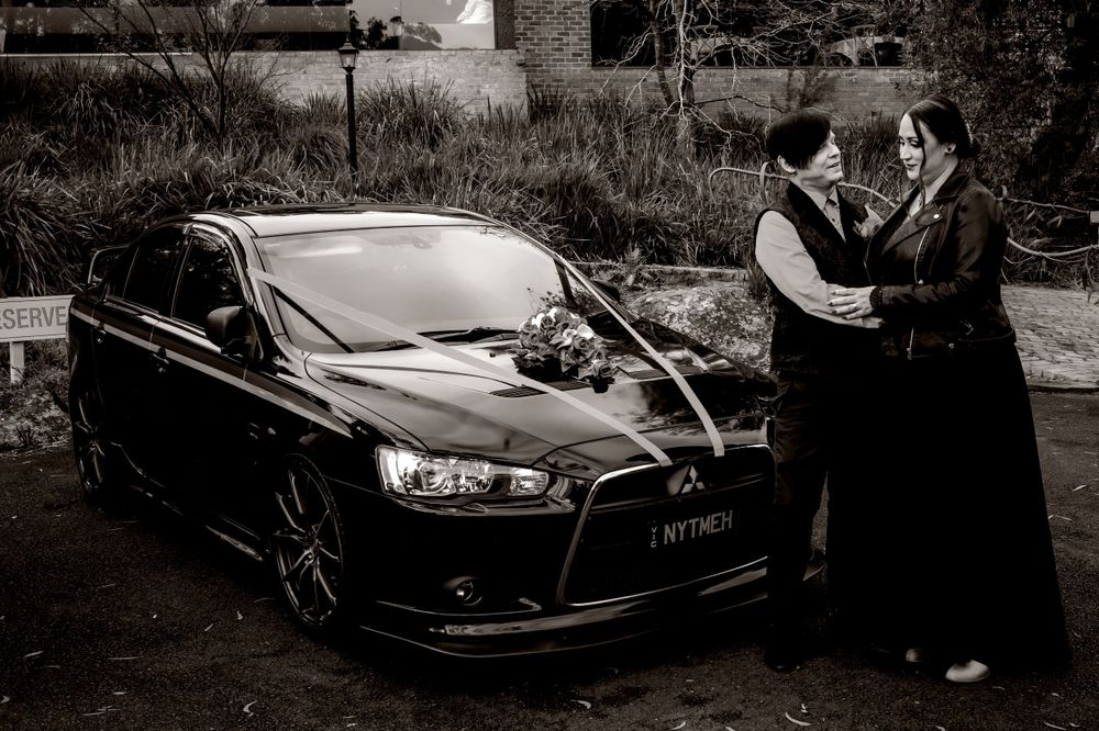 Bride in black dress and groom in black vest in car photoshoot series showing different angles of a classic automobile in black and white.
