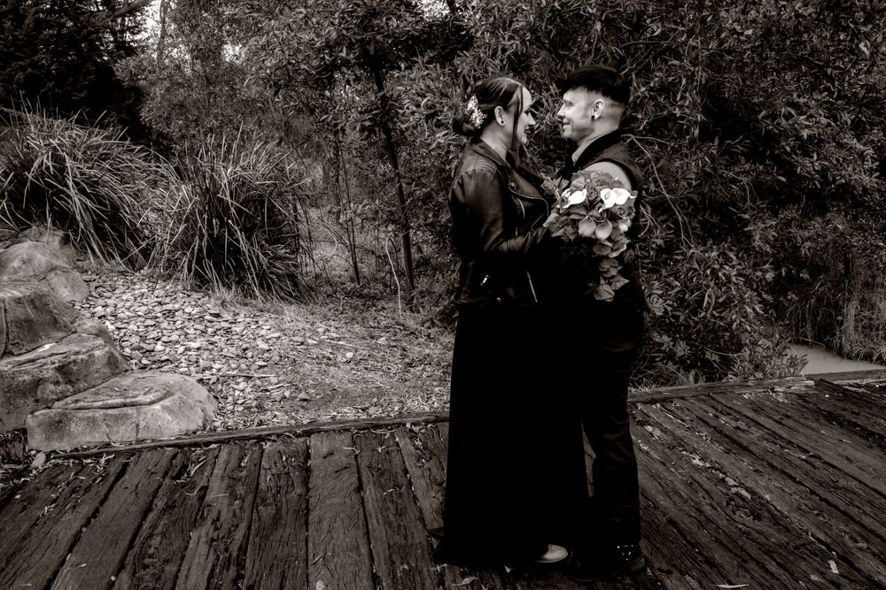 Bride in black dress and groom in black Dramatic black and white photo ln a wooded area with artistic silhouettes against natural backdrop.