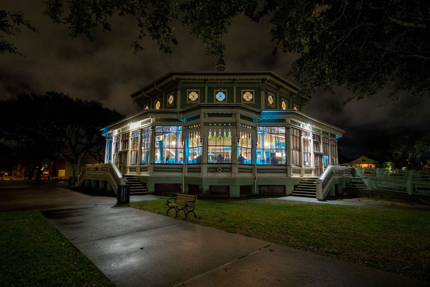 Historic glass pavilion lit up at night with glowing blue interior lights.