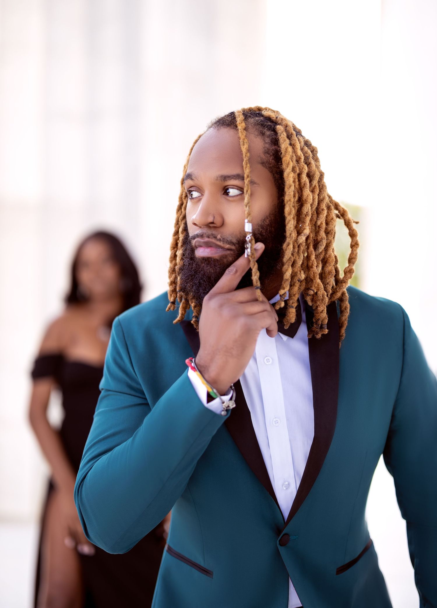 Portrait of a man in teal suit touching his face thoughtfully.